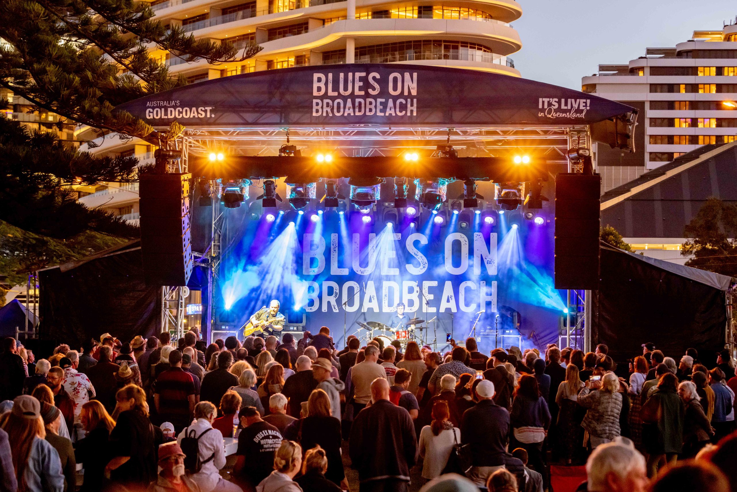 Festival stage with band playing in front of a large crowd under blue stage lights and Blues on Broadbeach backdrop.